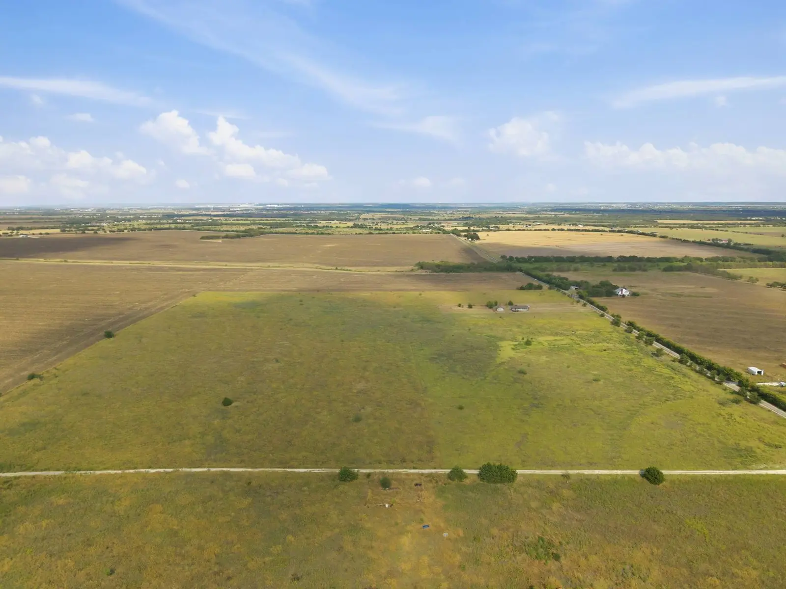 Aerial view of the property: open pasture under a wide Texas sky, with farmland stretching to the horizon